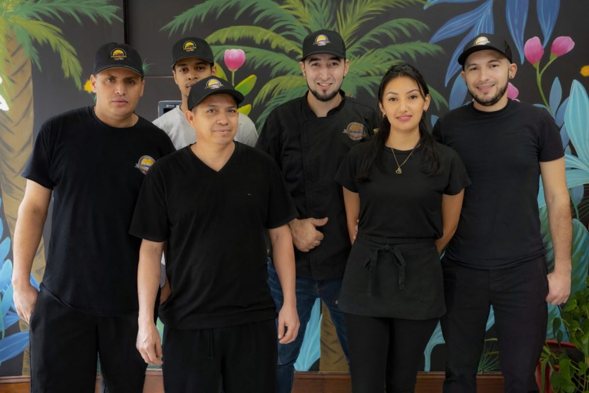 The Delicias Colombianas Hyde Park team photographed together in front of the restaurant mural